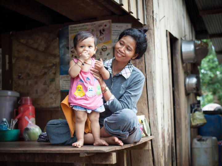 Khmer mother smiles as she holds up her baby toddler so she is standing 