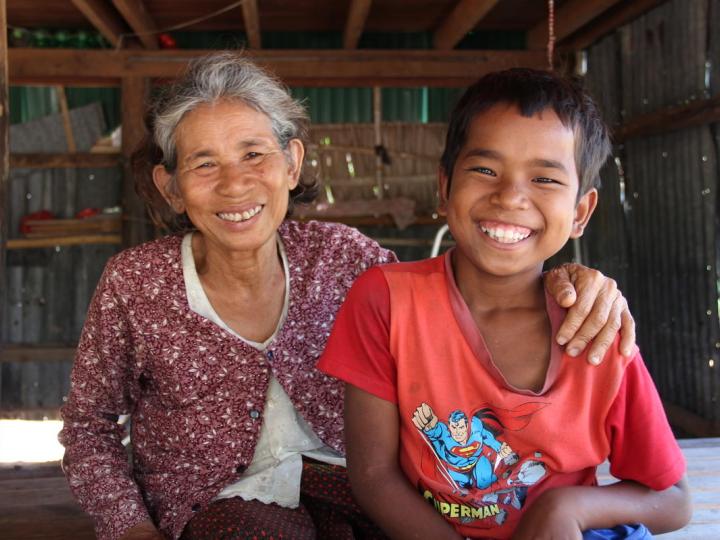 12 year old Khmer boy sits with his grandmother, they are both smiling at the camera.