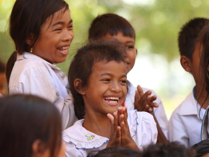Cambodian girl smiling with student peers around her all clapping their hands with joy.