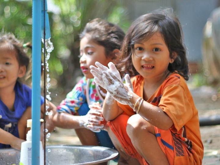 Three Khmer girls wash their hands in a bucket from a tap installed by World Vision Cambodia