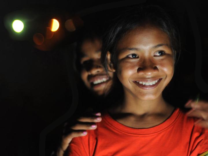 Two young Khmer women stand smiling, it is night time