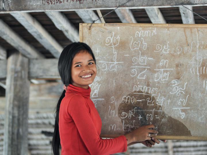 Khmer youth stands in front of blackboard with Khmer script teaching students at youth club, Cambodia