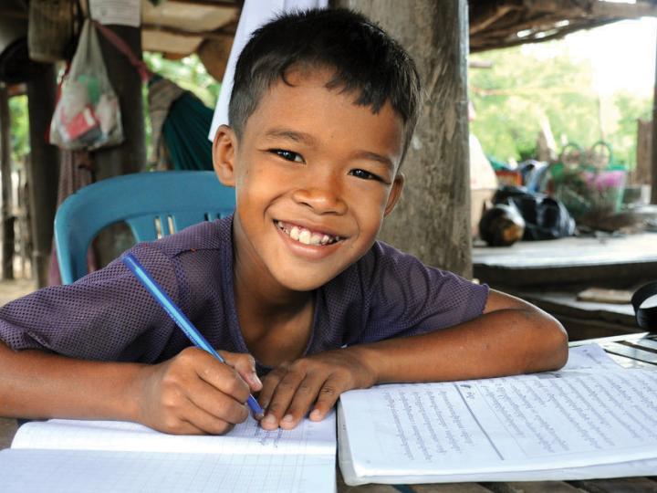Khmer boy smiles at the camera with pen in hand, writing in his school books, Cambodia.