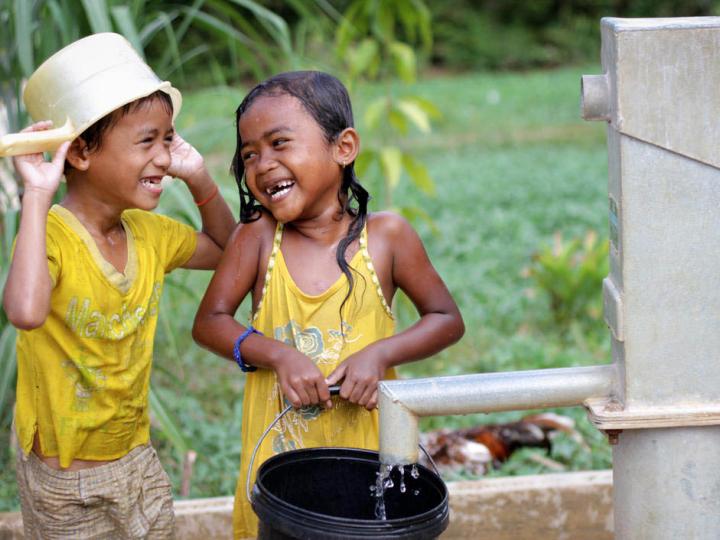 Khmer boy and girl laughing at each other playing in water from pump installed by World Vision Cambodia.
