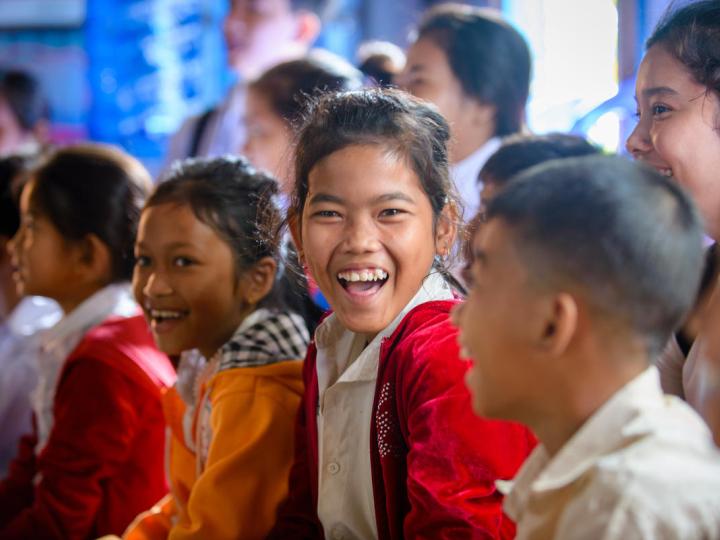 Group of Khmer children sitting on the floor of a classroom with one ecstatic girl looking directly at the camera