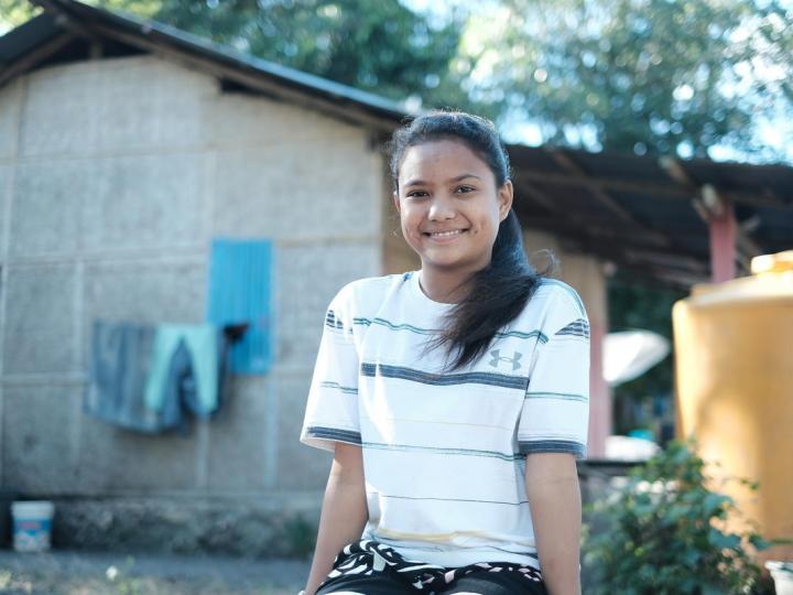 girl sits outside a house smiling