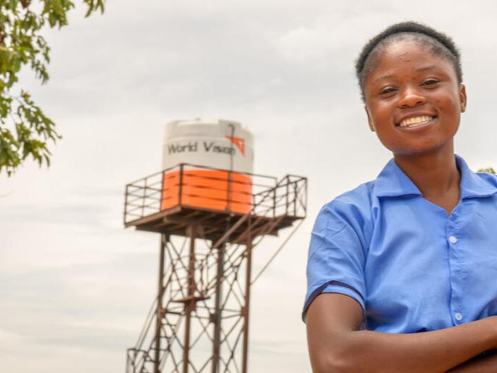 Viola, age 16, stands in front of the water tower at her school, Bulanda Primary School.