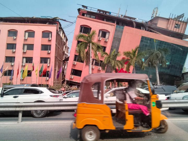 Orange vehicle drives past building damaged in Myanmar